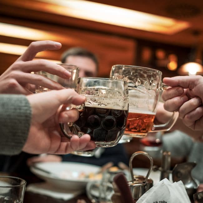 A close-up of a bartender's hands pouring a deep amber barrel-aged ale into a tulip glass at Flansk's taproom, condensation forming on the outside of the glass, warm low lighting in the background