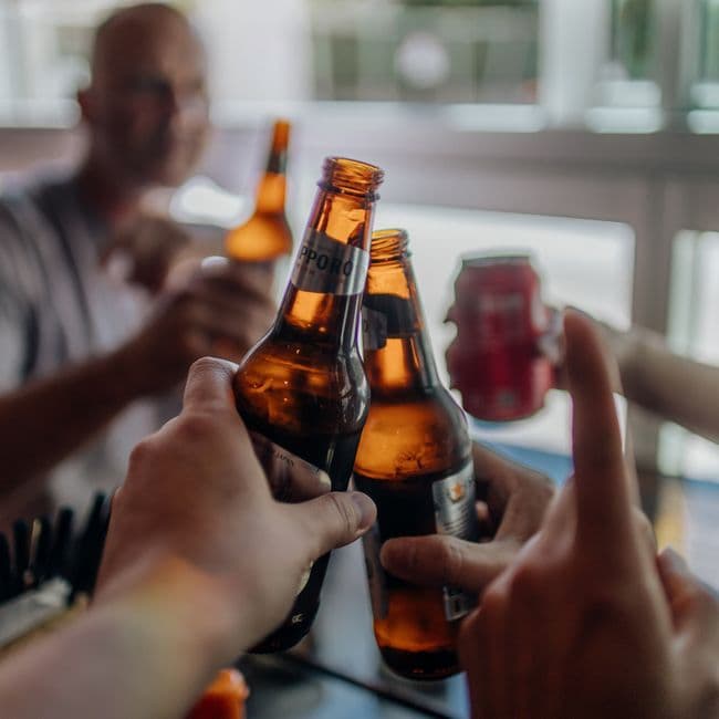 Two people in their early thirties leaning over a high wooden table at Flansk, reading a small printed release card next to their beers, mid-conversation and visibly engaged — not performing enjoyment, actually having it
